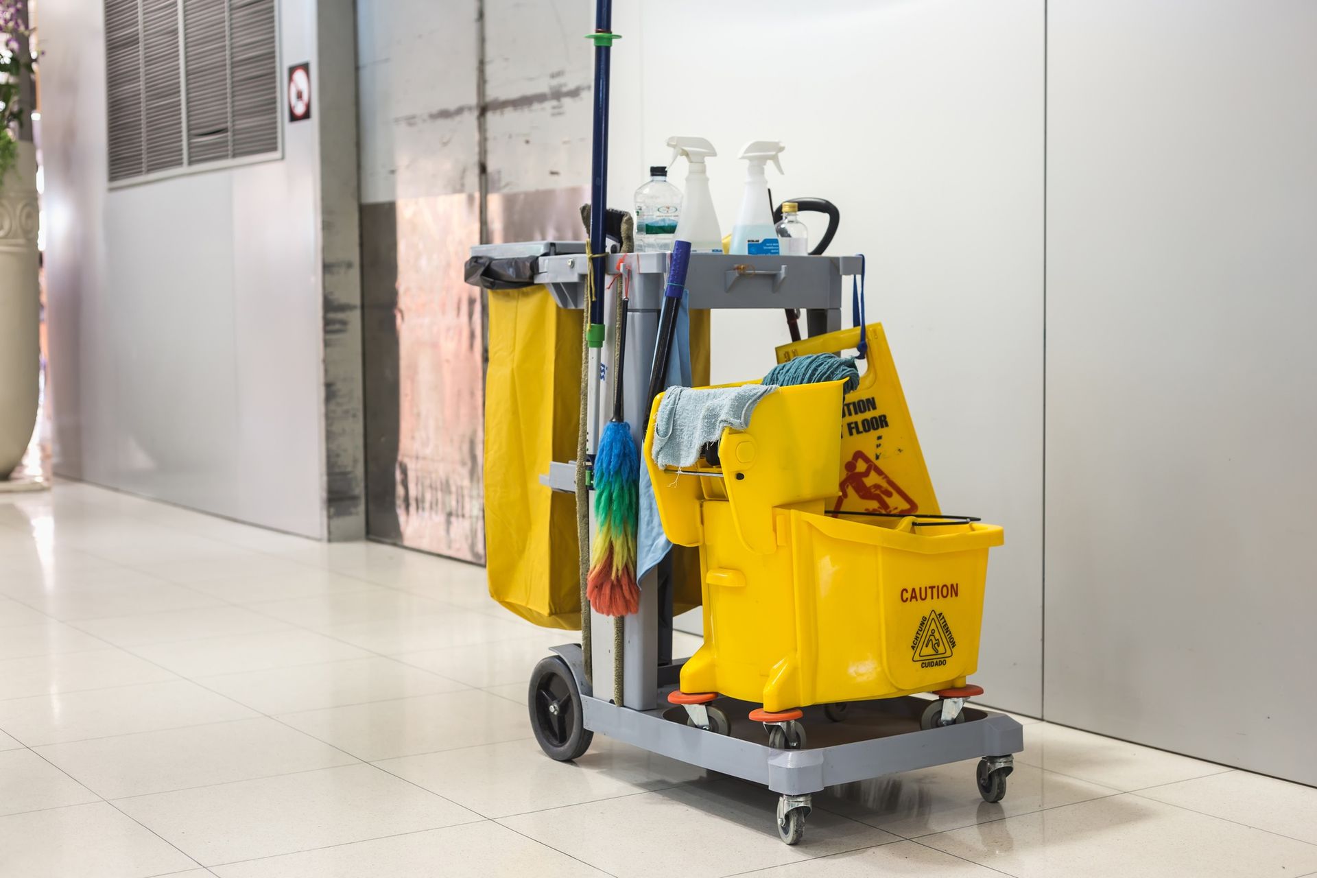 A cleaning cart is parked in a hallway next to a wall.