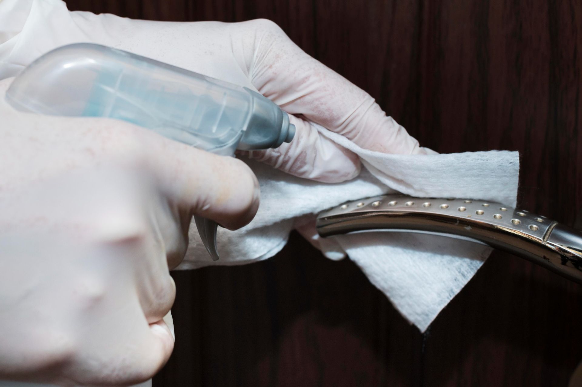 A person is cleaning a door handle with a spray bottle and a napkin.